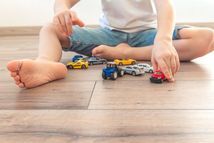 Laminate Flooring for Basements. Little Boy Is Playing With Colored Toy Cars At Home.