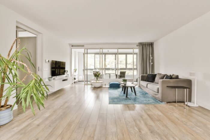 Hardwood Flooring. a living room with wood flooring and white walls, including a large plant in the center of the room.
