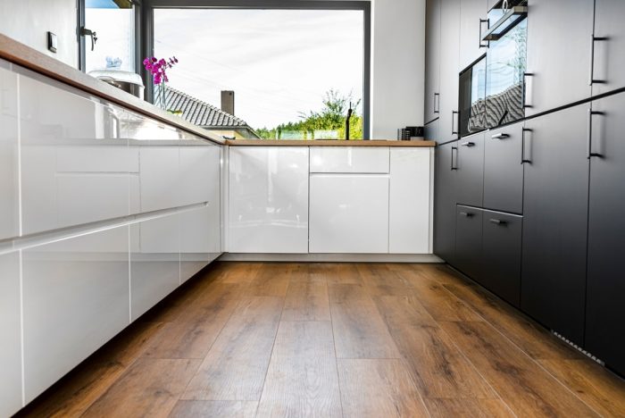 Luxury Vinyl Flooring. A modern kitchen with white and black fronts and a large corner window, vinyl panels on the floor.