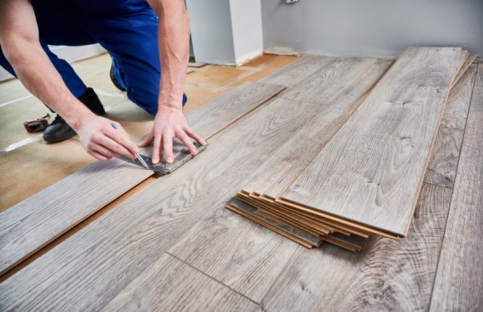 Laminate Flooring in Ottawa. Man preparing laminate plank for floor installation in apartment under renovation. Close up of male worker using metal construction ruler and pen while drawing line on laminate flooring board.