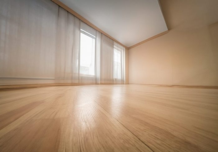 Flooring Solutions. Empty wooden floor closeup and room ceiling and doors with light reflection.