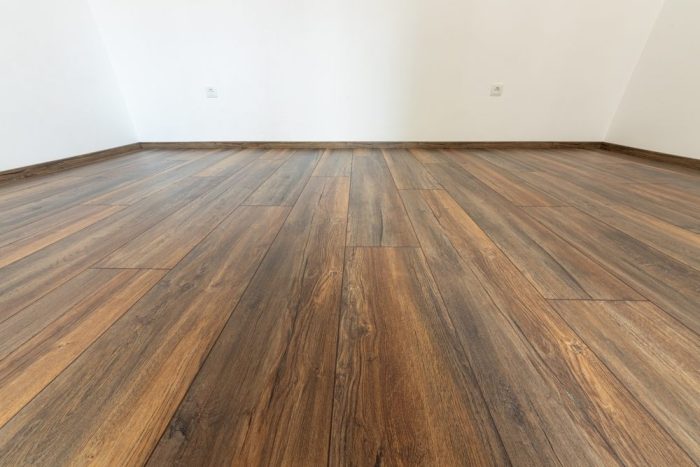 Why Visit Ottawa Diamond Flooring for Your Flooring Needs? Laminated wood floor with white wall. Empty room with floating laminate in new apartment.